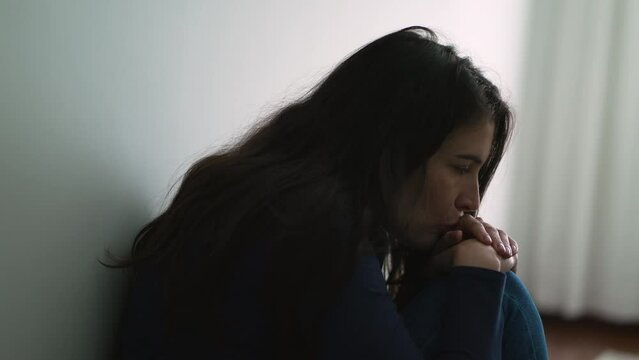 Pensive depressed woman sitting on floor at home leaning on wall pondering emotional problems