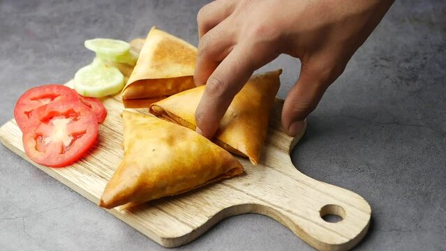 hand pick a samosa from a chopping board 