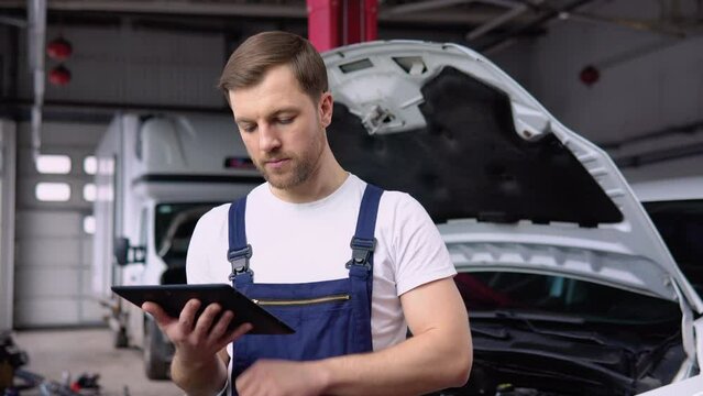 Professional car mechanic working in auto repair service with tablet. Computer diagnostics of the electric car in garage. Car maintenance service concept
