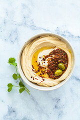 Homemade spicy hummus with tahini and olive oil in bowl, white marble background. Israeli traditional food.