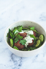 Green salad with falafel, tahini dressing in white bowl on white marble background. Alternative vegan recipe.