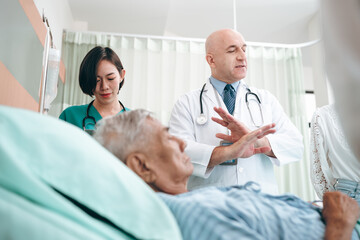 professional doctor standing by explain the treatment information via male elderly patient lying in bed in private hospital sickroom. The treatment program is suitable for people to socialize elderly