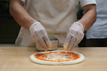 chef makes pizza with his hands putting the ingredients for the pizza on the table. The dark background.