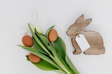Bouquet of fresh white tulips, brown eggs, and wooden rabbit. Background with Easter Bunny for...