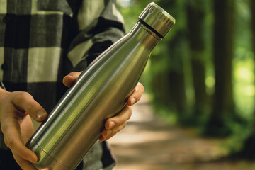 Close-up of Unrecognizable female hand holding Water bottle. Reusable steel thermo water bottle in...