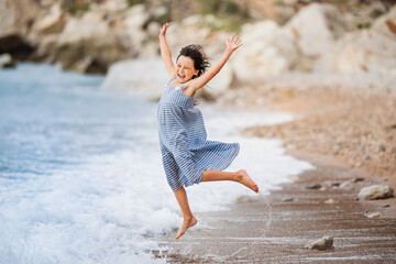 Happy child jumps into sea. Little girl is running on the beach.