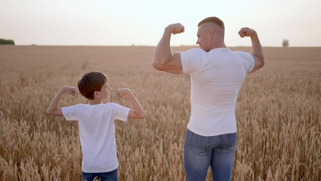 Father and son showing muscles biceps. Father man son boy child teenager having fun sunset sun summer field, Concept childhood friendship care healthy lifestyle sports activity happy family together.
