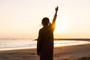 Silhouette of woman rise up the hand at sunset in the beach