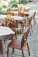 Chairs with hole pattern on backs and empty tables in open air restaurant on summer day. Cozy place for dinner on shady city street on seaside