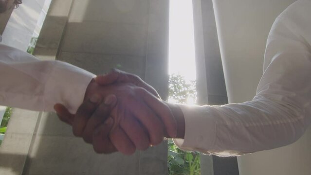 Close-up shot of two impersonal business partners shaking hands outdoors in front of the office building