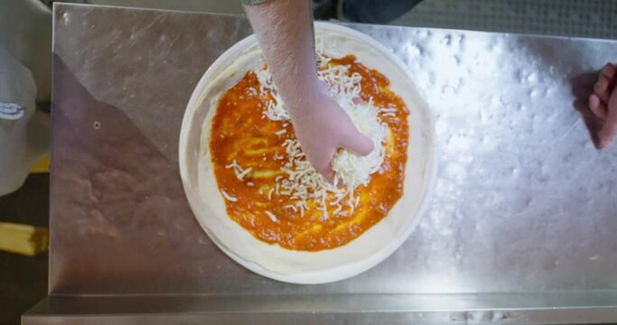 Making pizza from scratch with pizza sauce, cheese and sausage. mobile phone video, vertical video. Close up of hands making pizza.