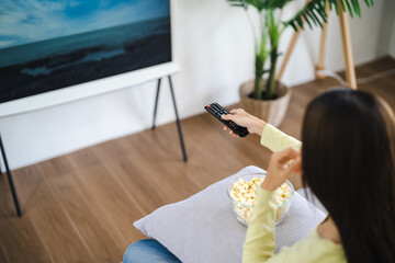 Asian woman Watching smart TV and using remote controller Hand holding television audio remote...