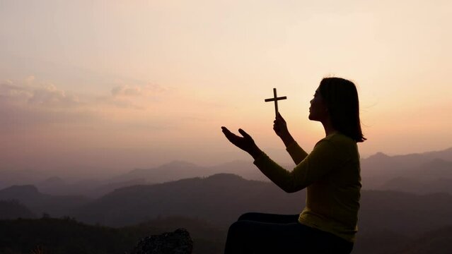 Silhouette of woman hands praying with cross  in nature sunrise background,  Crucifix, Symbol of Faith. Christian life crisis prayer to god.