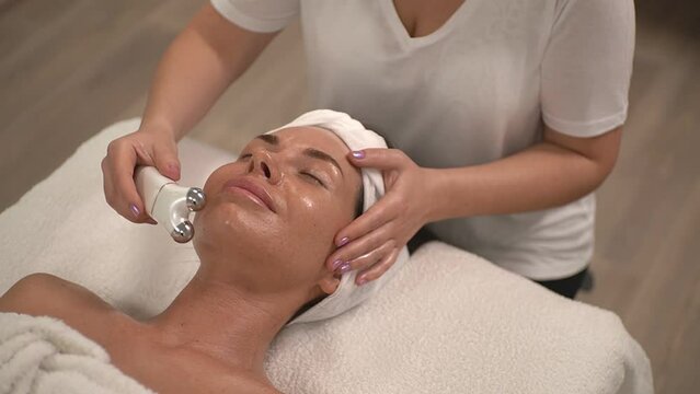 master woman in a white t-shirt performs a procedure using a microcurrent facial apparatus. real time video. High quality Full HD video recording