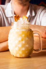 Pina colada cocktail with ice, pineapple chips, cocktail straw in glass with handle on wooden table, male man hands. Front view, close-up, vertical photo.