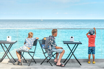 Obraz premium Brothers look at calm azure sea resting together in neat street cafe backside view. Cute boys spend vacation at popular seaside resort