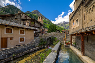 Fototapeta na wymiar Alpine creek among old houses in small town of Chianale, Italy.