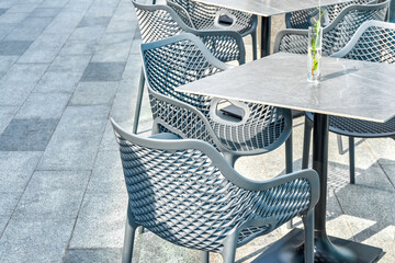 Comfortable plastic chairs and porcelain stoneware table with flower in glass vase on city street...