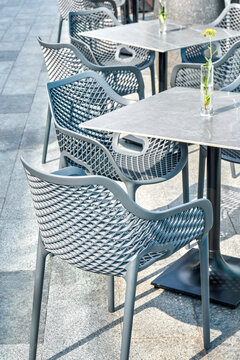 Comfortable plastic chairs and porcelain stoneware table with flower in glass vase on city street closeup. Furniture for restaurants and cafes