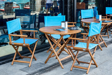 Wooden furniture with color fabric for guests near glass facade of cafe on city street. Comfortable place to rest for tourists in summer town