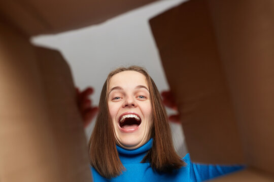 Extremely happy overjoyed woman customer wearing blue turtleneck opening parcel, looking inside package with cheerful joyful look, being glad to receive excellent present.