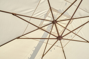 Light beige umbrella protects cafe visitors from sun beams close low angle shot. Accessory for public places decoration and atmosphere