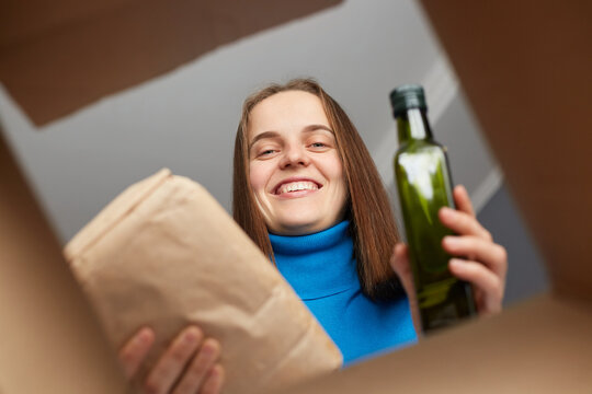 Smiling kind charming woman looking inside box, volunteer collecting food donations for the needs of Ukrainian migrants, getting grocery shopping, receive order of groceries.