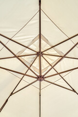 Light beige umbrella protects cafe visitors from sun beams close low angle shot. Accessory for public places decoration and atmosphere