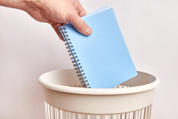 A used business notebook is thrown into the trash. Paper disposal and recycling.