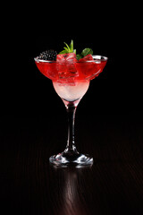 Rose-red sparkling iced cocktail garnished with blackberry and mint leaf. Side view, selective focus.