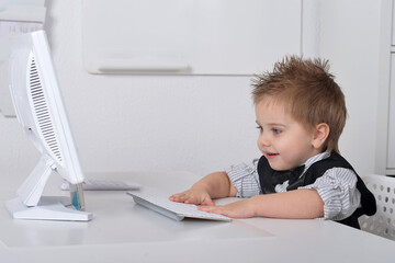 Fototapeta na wymiar Little handsome boy sits with a computer 