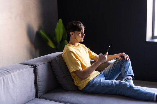 Content young man relax on sofa use smartphone spend free time online in social network chat at web app play easy game online.