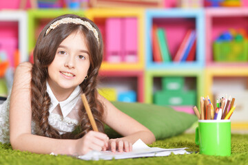 Beautiful little girl draws with a pencil on a sheet of paper 