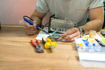 The young master electronics engineer checks, repairs and finishes the motherboard he was given to repair. He uses his tools and works in a home environment.