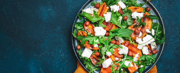 Summer salad with grilled peach with soft cheese, hazelnuts and arugula on blue table background,...