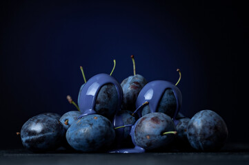 Ripe blue plums piled up. Two plums covered with blue glossy paint. Colorful bright fruits. Dark blue background. Side view. Copy space. 