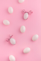 Cute Easter flat lay background with white eggs and satin ribbon on pink background