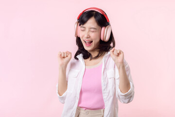 Smile pretty asian model person listen music song and enjoy dance with wireless headphone online audio radio sound. Positive fun exited joyful youth female woman on pink isolated background studio