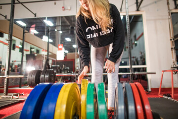 Young woman selects barbell weights from the weight rack at the gym