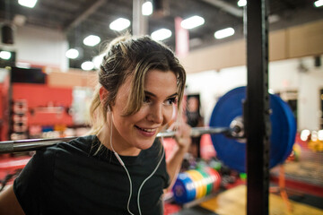 Smiling woman weight lifting with barbell in gym