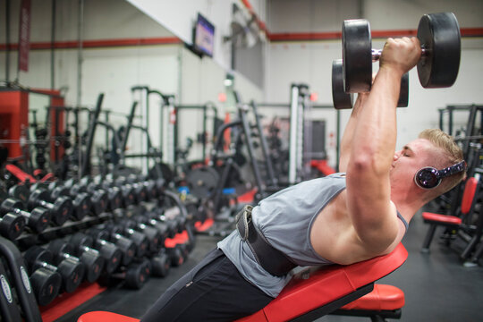 Fit millennial training pectoral muscles with dumbbells at the gym