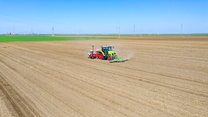 Aerial view of tractor as dragging a sowing machine over agricultural field, farmland