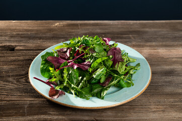 salad mix of fresh herbs, arugula, Swiss chard, spinach in tarenle on a wooden background, top-side view