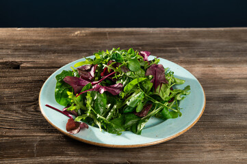 salad mix of fresh herbs, arugula, Swiss chard, spinach in tarenle on a wooden background, top-side...