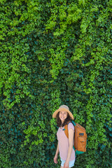 A girl in a straw hat stands near a wall overgrown with ivy