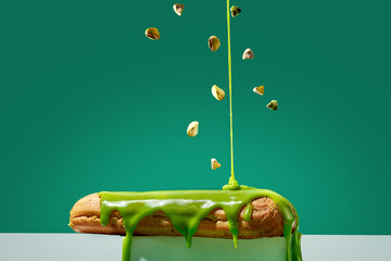 Pistachio eclair is poured with glaze and sprinkled with pistachios on a green background.