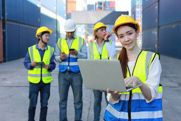 Group of multiethnic technician engineer in protective uniform standing and using computer, walkie talkie radio and tablet while.working together and controlling at container cargo site industrial
