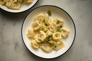 ready hot ravioli with pesto sauce and grated cheese on a white plate close-up. dumplings ready to eat	
