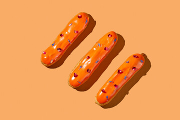 Three eclairs with orange glaze and custard on an orange background. Creative layout. Creative food poster