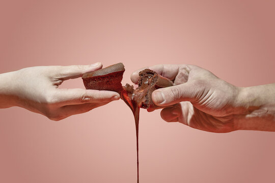 A female and a male hand have broken the chocolate fondant with the filling flowing out. brown background